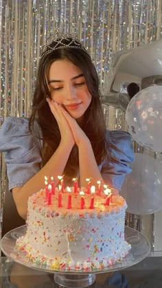 a woman sitting in front of a birthday cake with lit candles on it and her hand near her face