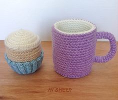 two crocheted coffee mugs sitting on top of a wooden table next to each other