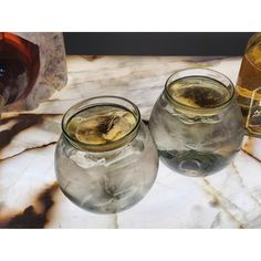 three glasses filled with liquid sitting on top of a marble table next to two bottles