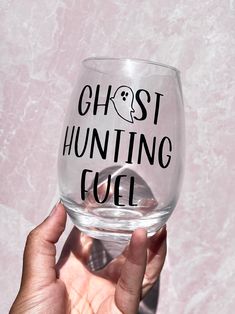 a hand holding up a wine glass that says ghost hunting fuel on the bottom and black lettering