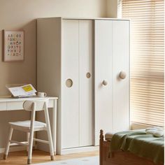 a bedroom with a bed, desk and white cupboards in front of a window