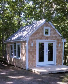 a small wooden cabin in the woods with doors open and windows on it's side