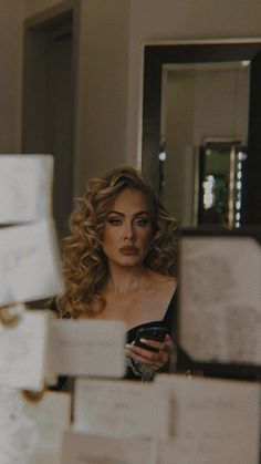 a woman looking at her cell phone in front of stacks of boxes and papers on the wall