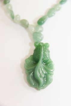 Hand carved big green glass Koi fish pendant dangling from small green Aventurine/jade nuggets necklace. 16" Whimsical Hand-Carved Glass Green Koi Fish Pendant: The Asian Koi fish is very spiritual and very lucky in all aspects of your life. Koi fish is the Chinese symbol of good luck, prosperity, & Tranquility. According to Feng Shui, a fish represents wealth and prosperity because the actual word in Chinese for fish, in Pinyin: yú, 魚, also translates to “abundance” The color green associated with the heart chakra is Green. Green symbolizes harmony, creativity, health, abundance and nature. Green Aventurine: Aventurine meaning comes from the Italian word Aventura which means chance, a hint at the great fortune this stone can bestow upon you. Aventurine is a stone of prosperity. It reinfor Green Hand-strung Amulet Jewelry, Spiritual Green Jade Necklace, Green Jade Spiritual Necklace, Spiritual Single Strand Jade Necklace, Green Jade Amulet Necklace, Green Aventurine Amulet Jewelry, Spiritual Jade Necklace For Good Luck, Unique Green Carved Necklace, Green Jade Necklace With 108 Beads