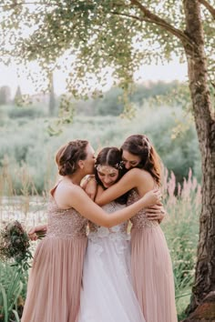 three bridesmaids hugging each other in front of a tree