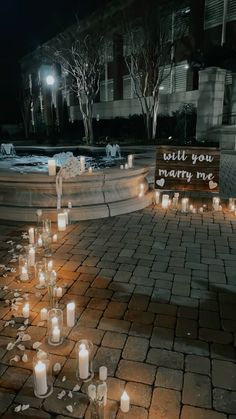 many lit candles are on the ground near a sign that says will you marry me?