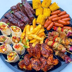 a platter filled with meats, vegetables and corn on the cob sticks