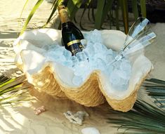 a bottle of champagne sitting on top of a basket filled with ice and sand next to palm leaves