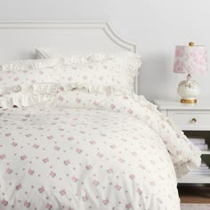 a white bed with pink flowers and ruffled bedspread on top of it