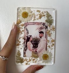 a hand holding a glass photo frame with flowers on it