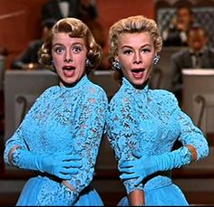 two women in blue dresses standing next to each other with their hands on their hips