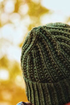 a person wearing a green knitted beanie looking at something in the distance with trees in the background