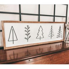 a wooden sign with trees drawn on it sitting next to a vase and planter