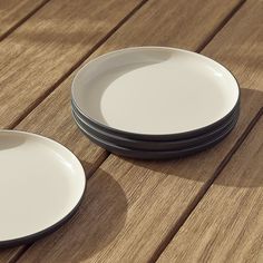 three white plates sitting on top of a wooden table next to each other with black rims