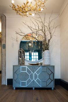 a room with a mirror, vases and branches on the sideboard in front of it