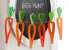 paper carrots are hanging from a string on a chalkboard with the word egg hunt written above them