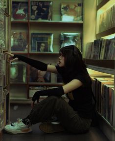 a woman sitting on the floor in front of a bookshelf with her arm outstretched