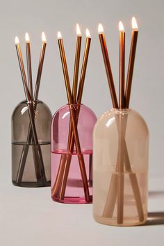 three vases with candles in them on a white surface, one is pink and the other two are brown