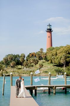 a bride and groom standing on a dock in front of a light house