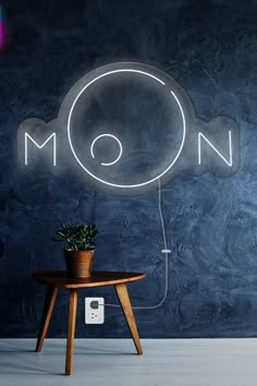 a neon sign that reads moon above a table with a plant on it and an ipod charging in front of it