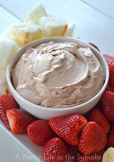 a white bowl filled with chocolate frosting next to strawberries