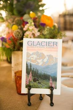 there is a place card holder on the table with flowers in the vase behind it