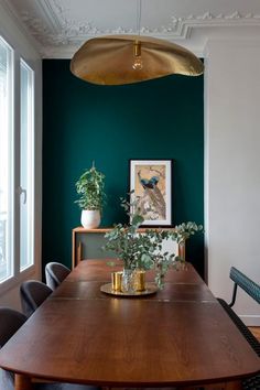 a dining room with green walls and wooden table surrounded by chairs, potted plants