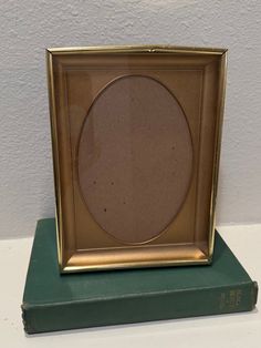 a gold frame sitting on top of a green book with a white wall in the background