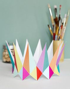 three colorful paper crowns sitting on top of a table next to pens and pencils