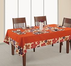 a dining room table with an orange flowered tablecloth and matching wooden chairs in front of large windows