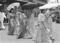 an old black and white photo of women in dresses with umbrellas walking down the street