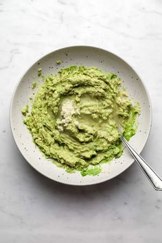 a white bowl filled with guacamole on top of a marble countertop