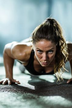 a woman is doing push ups on the floor with her hands behind her head and looking at the camera