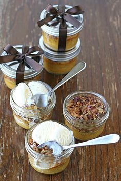 four jars filled with desserts on top of a wooden table