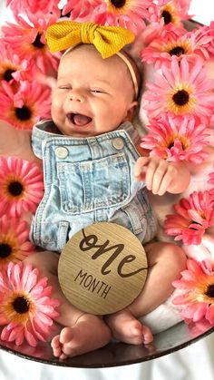 a baby in overalls and a yellow bow is holding a sign that says mom