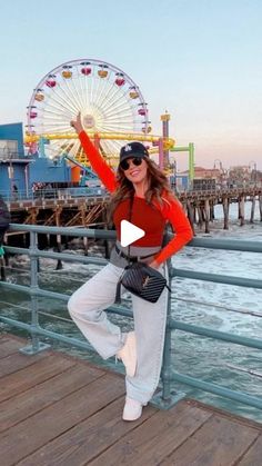 a woman standing on top of a pier next to a ferris wheel