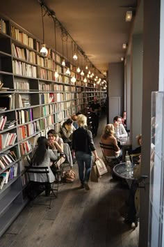 people sitting at tables in a library with lots of bookshelves and lamps hanging from the ceiling