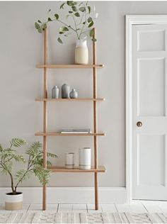 a wooden shelf with vases and plants on it in front of a white door