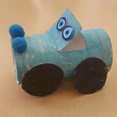 a blue paper toy with eyes on it's face and wheels, sitting on a table