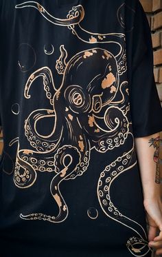 an octopus t - shirt is being held by someone's hand in front of a brick wall