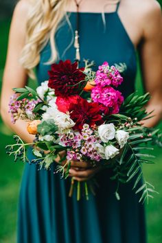 a woman in a blue dress holding a bouquet of red, white and pink flowers