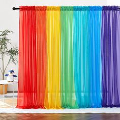 a rainbow colored curtain hanging in front of a white table and potted plant next to it