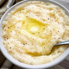 a bowl filled with mashed potatoes covered in butter and seasoning next to a spoon