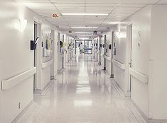 an empty hospital hallway with white walls and doors leading to the rooms on each side