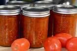 tomatoes and other vegetables sit in jars on a table