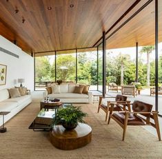 a living room with couches, chairs and tables in front of large windows that look out onto the trees