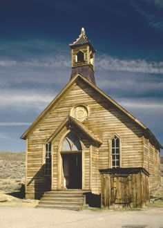 an old wooden church with a steeple and clock on the front, sits in a desert landscape