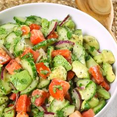 a white bowl filled with cucumber, tomatoes and red onion salad on top of a table