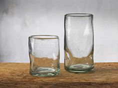 two glass vases sitting on top of a wooden table next to eachother