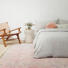 a bed sitting next to a wooden chair in a bedroom on top of a rug